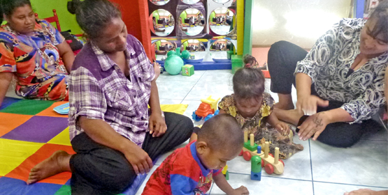 Two-year-old Lelos Jerbal and three-year-old Ruth develop thinking and fine motor skills putting rings on a stick and learning the sign for “on” with Chinilla Peter (right) and family members. Chinilla Peter named Act Early Ambassador