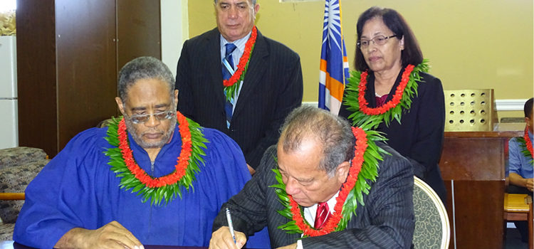 RMI Ambassador to Japan Tom Kijiner signs diplomatic papers after he took the oath of office at a ceremony at the ICC recently as High Court Chief Justice Carl Ingram (sitting), and (standing) Foreign Minister John Silk and President Hilda Heine look on. Photo: Hilary Hosia Kijiner reappointed to serve RMI