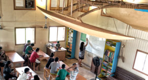 A traditional canoe built by the Waan Aelon in Majel (Canoes of the Marshall Islands) team soars above the WAM classroom, where a group of 25 trainees is engaged in the latest six-month vocational and life skills training.