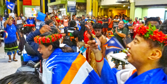 Enthusiastic friends, family and fans of RMI Micronesian Games athletes and coaches turned out in large numbers at Amata Kabua International Airport Sunday night to welcome the basketball teams back from Yap. Both teams won silver medals at the 9th Micro Games. In the foreground decked out with RMI flags are women’s basketball standouts Jessica Olson (left) and Lulu Lejjena. Photo: Hilary Hosia Raucous fans greet Games athletes
