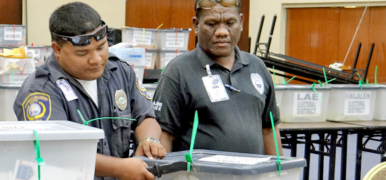 National police officer Artor Hesa (left) and local police officer Atran Jejon initiated the vetting process for postal absentee ballots Tuesday December 1 at the ICC tabulation headquarters by cutting open the zip-tied postal ballot storage containers. Photo: Hilary Hosia All eyes on RMI postal vote