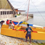 Waan Aelon in Majel Director Alson Kelen, left, with the WAM team as they pull the new-design catamaran onto the shoreline in front of the canoe program in Majuro. Photo: Eve Burns.