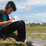 MIHS student Willy Abraham did his Upward Bound class assignment on the ocean side reef outside of his CMI classroom after a power outage hit the Uliga campus. Photo: Wilmer Joel.