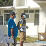 A USAG-KA official outfitted in full body personal protection equipment stands with three Marshallese who returned to Kwajalein from Pohnpei May 28: Godfrey Capelle, Benjamin Thomas and Connielynn Paul. They are standing outside housing that they are using for a 14-day quarantine period before they can return to Ebeye. Capelle and Thomas were lost at sea for 42 days until they drifted into Namoluk Atoll in the FSM May 14. Photo: Hilary Hosia.