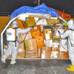 In the photo, RMI EPA’s Aaron Langinlur and Paul Paul are spraying disinfectant on dry cargo coming into RMI by plane at Amata Kabua International Airport in Majuro. Photo: Louie Sailas.