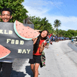 A parade of students and teachers from Alwal (end of Rita) to Marshall Islands High School celebrated World Food Day, while giving everyone some outdoor exercise as part of World Food Day, a field day and teacher appreciation combined into one big day last Friday. MIHS students Bill Lorennij, holding the poster, and Susan Ned taking a selfie behind him as the parade stretches out behind them. Photo: Wilmer Joel