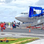 ‪Former First Lady Arlin Tomeing (left, top) is greeted on arrival Tuesday at Amata Kabua International by Ministry of Health and Human Services staff in full PPEs. She is among seven fully vaccinated people quarantining at Arrak, while 36 others are in quarantine at Kwajalein. Photo: Hilary Hosia/Office of the Chief Secretary.