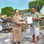 With debris from the recent fire that destroyed the Waan Aelon in Majel workshop and main office as a backdrop, Australian Embassy Deputy Chief of Mission Katrina Murray hands over a $20,000 donation to WAM Deputy Director Tony Alik. Photo: Eve Burns.