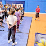 Newly arrived volleyball coach Francis Vicente, top right in red shirt, with the men’s and women’s teams last week at the ECC gym. Sports and Extracurricular Program Director Pranson Eliou is at right with clipboard, and coach Edison Mathusla. Photo: Giff Johnson.