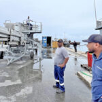 As engineer Shafick Hector extends the long arm of the tuna loader’s conveyor system, engineer Ricardo Christians and MIMRA’s Chief Fisheries Officer Beau Bigler look on at the PII dock Tuesday morning. Photo: Giff Johnson.